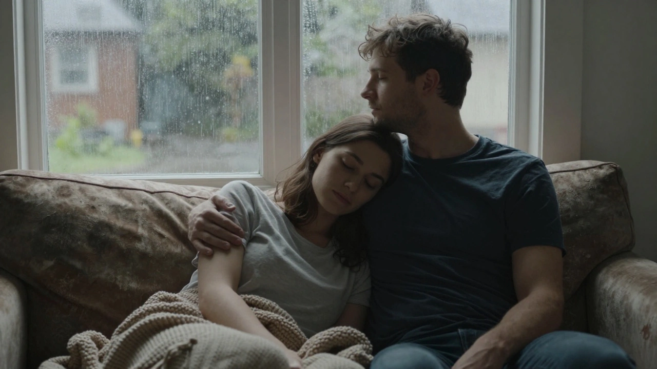 Een man en vrouw zitten op de bank, zij met haar hoofd op zijn schouder, regen op het raam—een moment van rust zonder woorden.